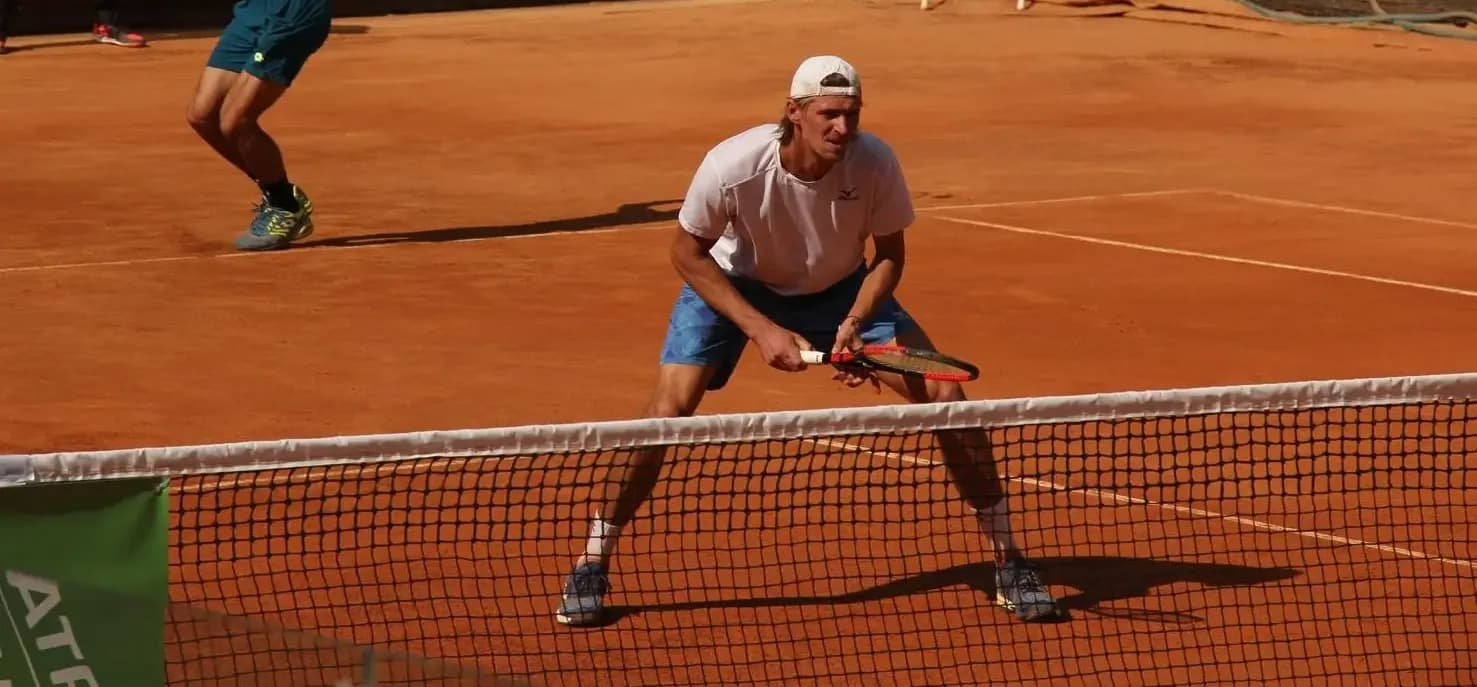 Alexander Bury, co-founder of ATN Tennis, at the net on a clay court